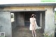 A naked woman in a white dress and straw hat standing in an abandoned building.