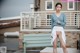 A woman in a blue sweater and white skirt posing on a bench.